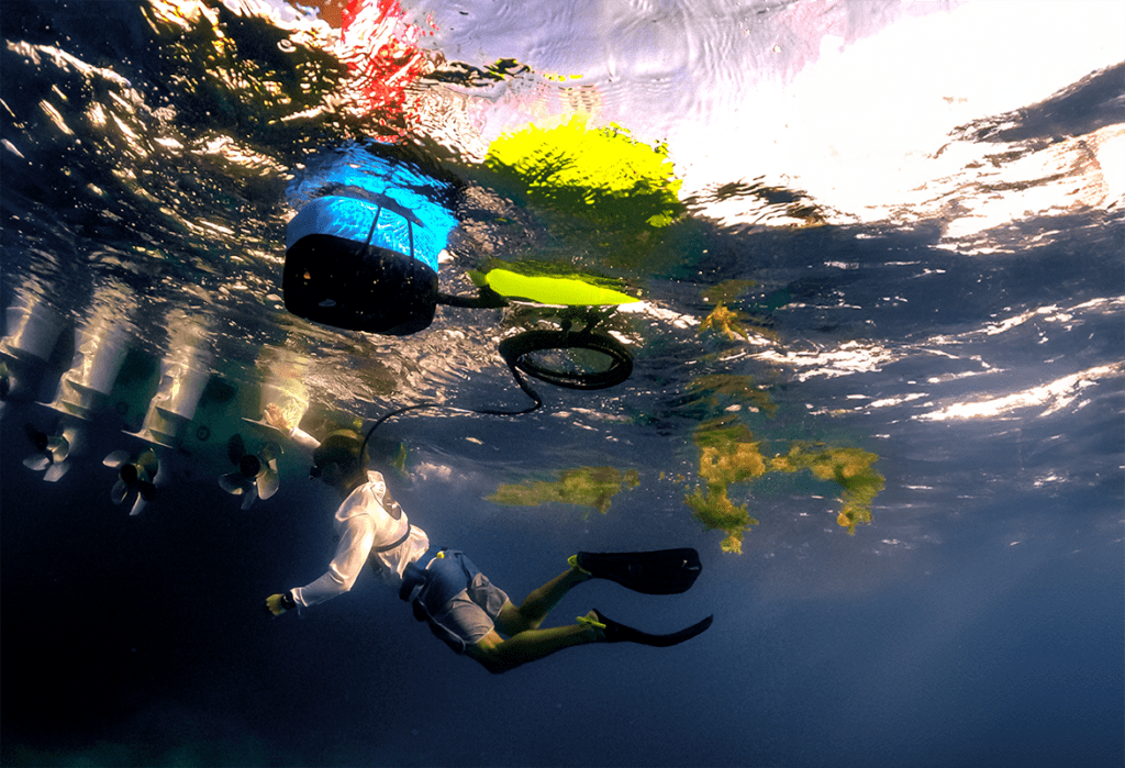 Diver inspecting a boat propeller underwater using the BLU3 Nomad Mini dive system, with the system hose extending from the surface.