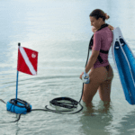 Diver standing in shallow water next to the Nomad battery-powered dive system with a dive flag.