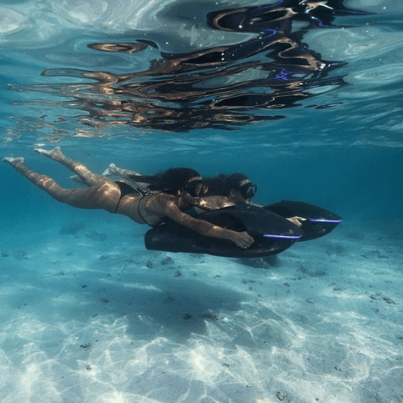 Two divers gliding underwater using SeaNXT Elite underwater scooters, showcasing the scooters' sleek design and low buoyancy for easy diving.