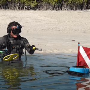 A person searches for treasure in the water using a metal detector while breathing from a BLU3 portable tankless dive system acting as a diving ventilator.