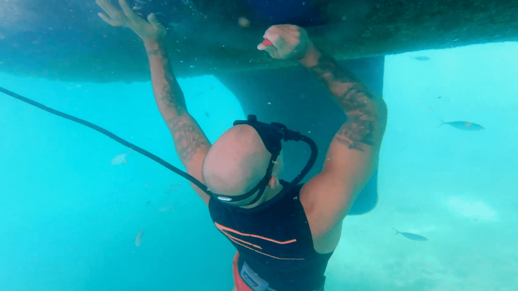 A diver cleaning the hull of a boat using the BLU3 Nomad dive system. The diver is breathing through the Nomad hose while inspecting and working underwater.