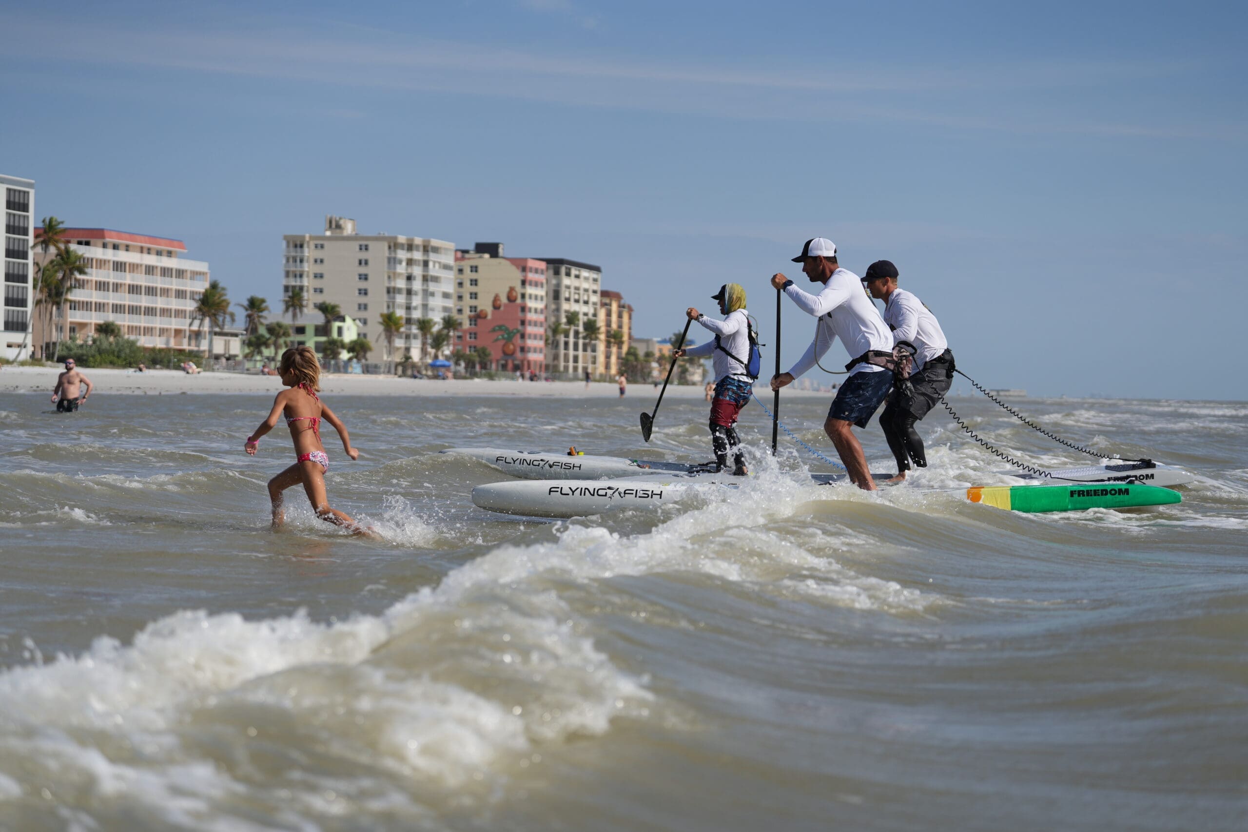 Finish line of the Florida Crossing Paddle in 2024 Three stand up paddleboarders riding into the beach in Fort Myers, Florida after just paddling 4 days across the state for a fundraiser to protect Florida waterways.