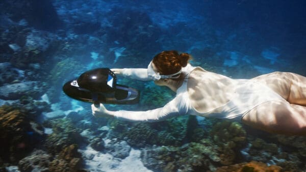Woman using Sublue Vapor underwater scooter to explore coral reef in clear ocean