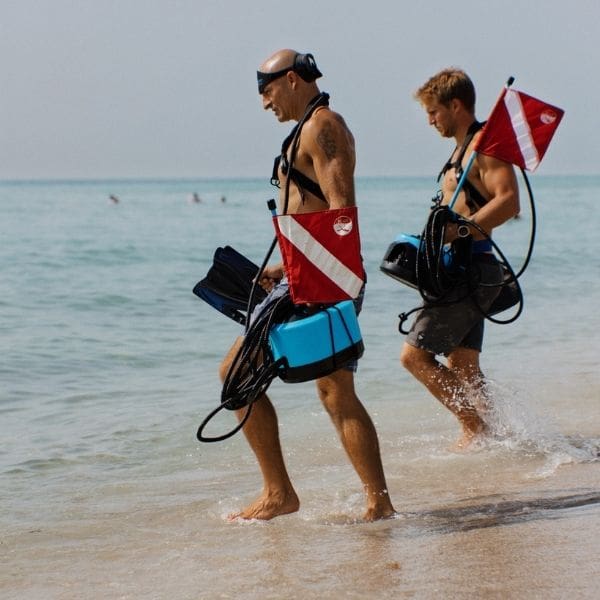 Two divers walk into water with BLU3 Nomad tankless diving system which is an alternative to snuba diving equipment.
